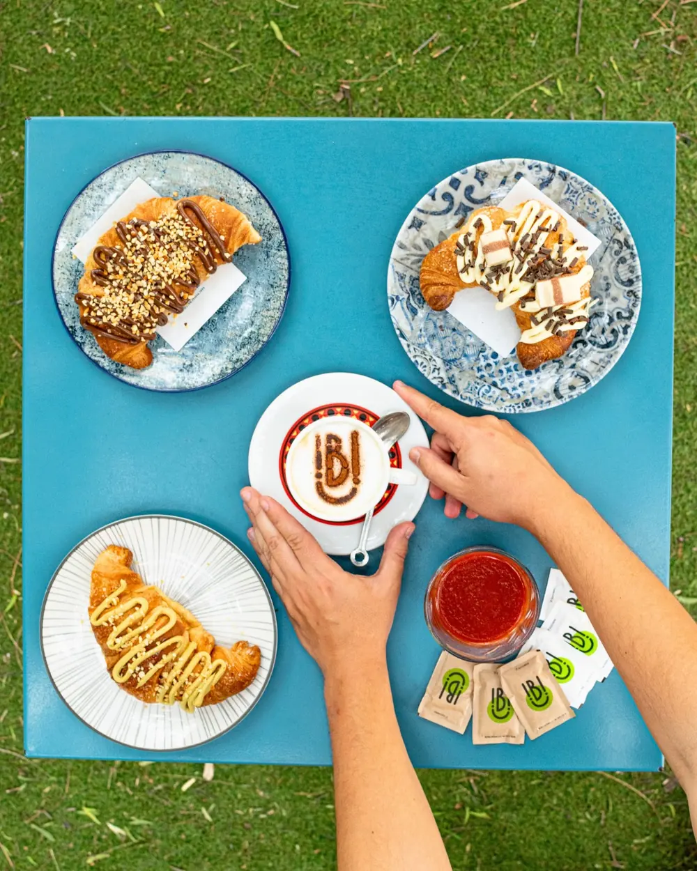 Tavolo azzurro con tre cornetti farciti, un cappuccino decorato con il marchio del locale e una spremuta