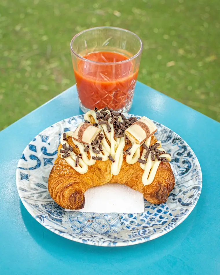 Cornetto farcito con crema al cioccolato bianco e cioccolatini, accanto a una spremuta