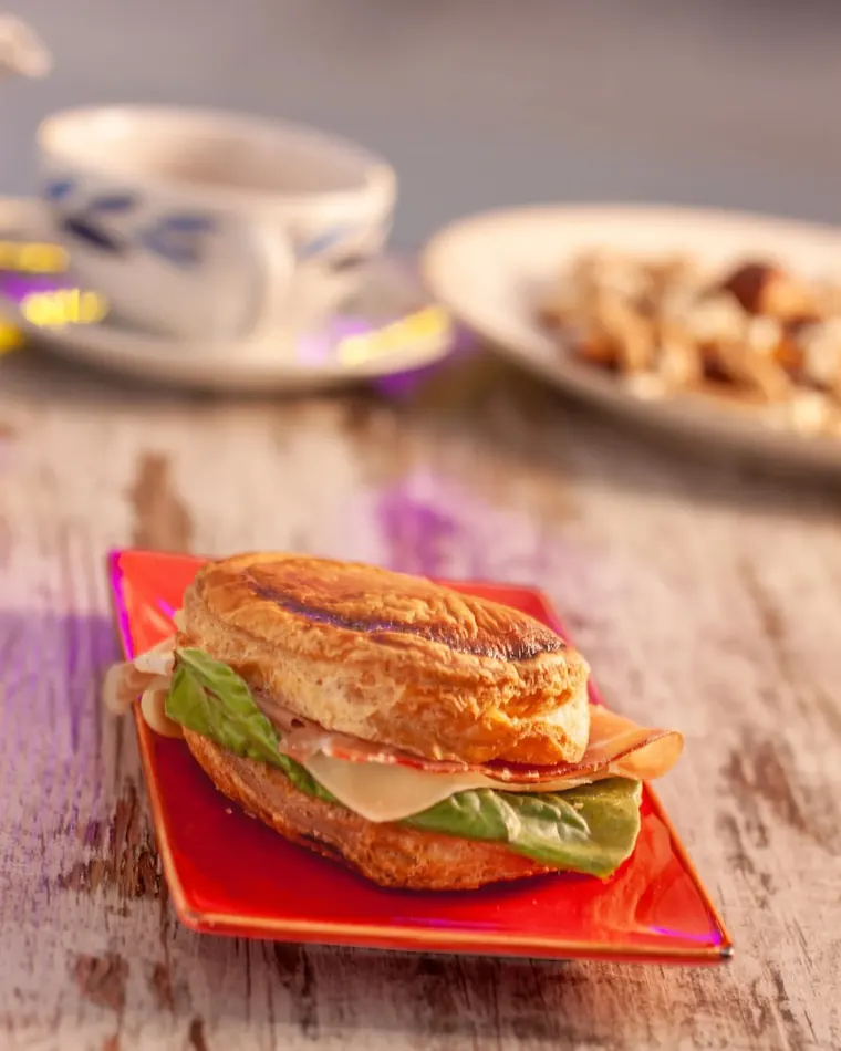 Croissant salato con prosciutto cotto, formaggio e insalata su un piatto rosso