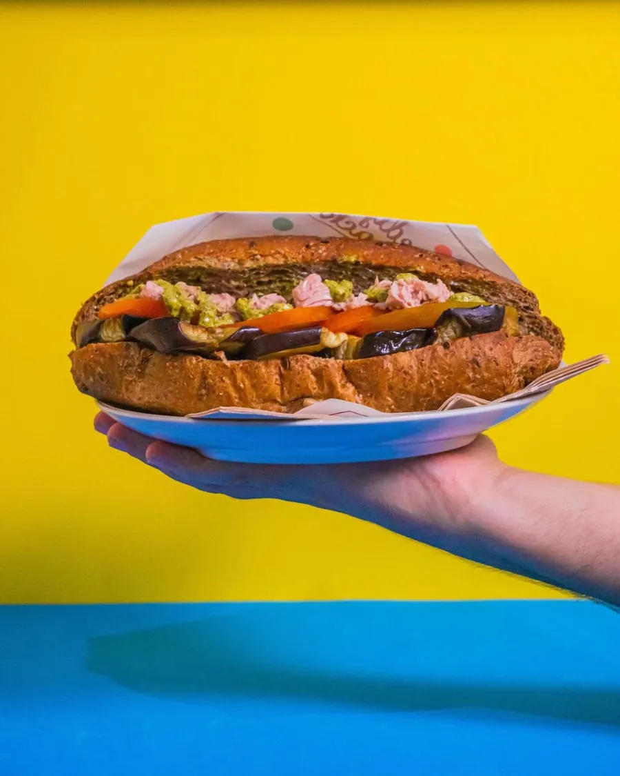 Panino con pane ai cereali, melanzane grigliate, pomodoro e pesto servito su un piatto azzurro