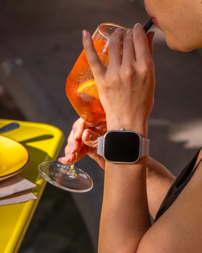 Calice di spritz tenuto in mano al sole, sopra un tavolino giallo