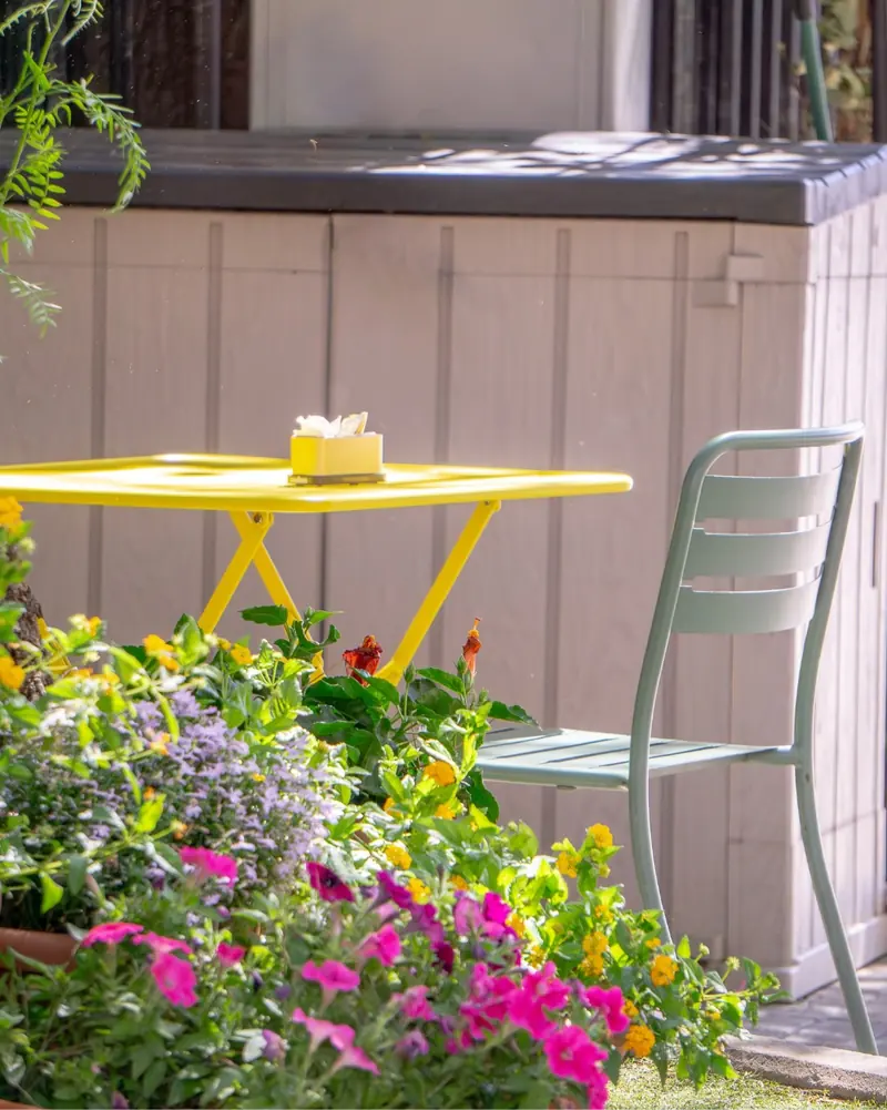 Tavolino giallo e sedia verde salvia circondati da petunie fucsia e fiori gialli