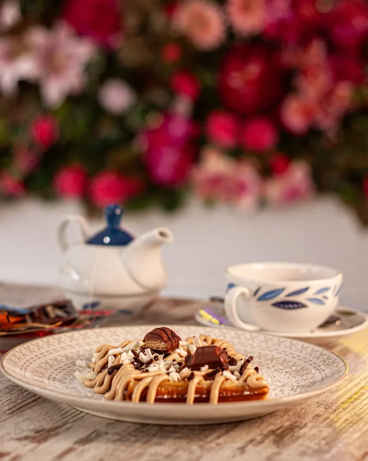 Waffle decorato con crema e cioccolatini, servito con teiera e tazza